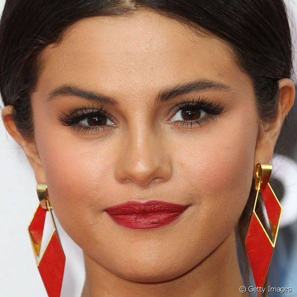 Selena Gomez usou um discreto esfumado marrom e completou o visual com batom vermelho combinando com seus brincos
